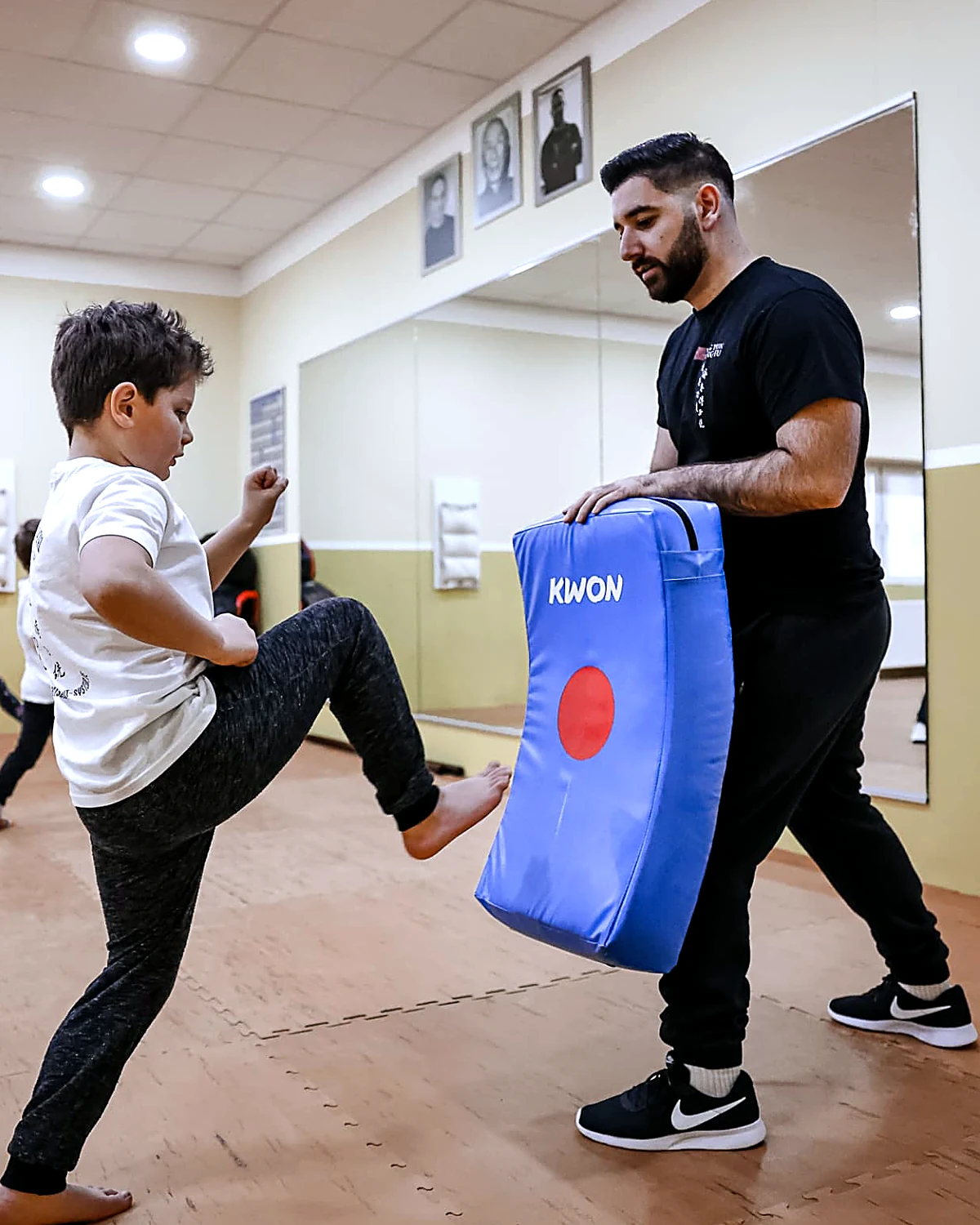 Jugendlicher tritt im Ving-Tsun-Training gegen das Schlagpolster, das der Trainer hält