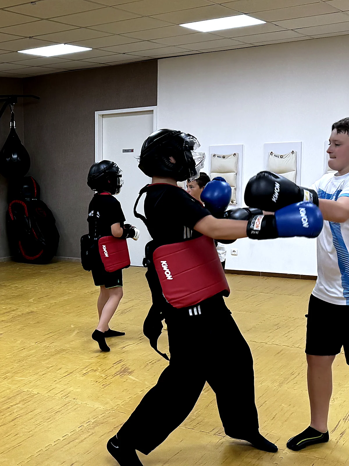Jugendgruppe trainiert paarweise mit Handschuhen und Pratzen im Saal